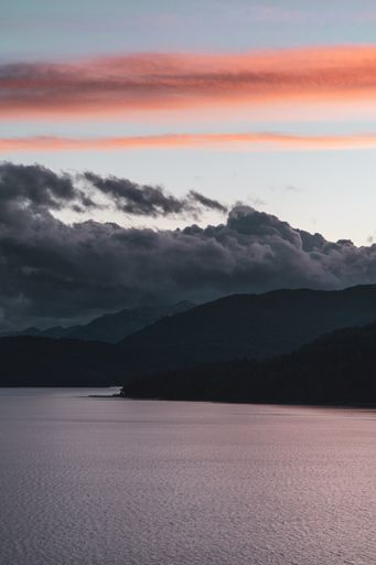 A vertical shot of a aesthetic cloudy orange sunset over mountains and a lake