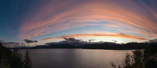 A panoramic shot of a aesthetic cloudy orange sunset over mountains and a lake