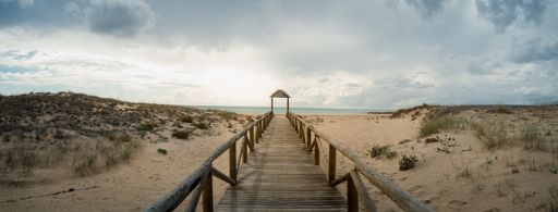 A wooden long platform leading to the beach under the cloudy sky