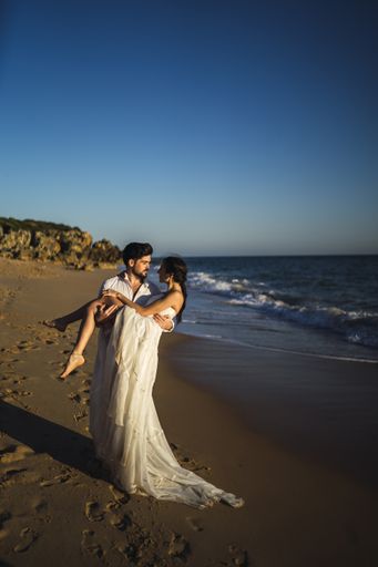 A vertical picture of a beautiful couple on their wedding day against a wavy ocean