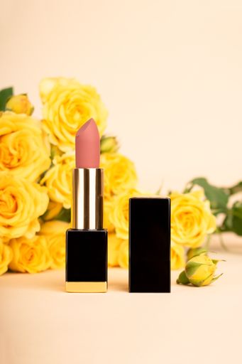 A vertical shot of pink lipstick and yellow flowers on the bright background