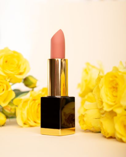 A vertical shot of pink lipstick and yellow flowers on the bright background