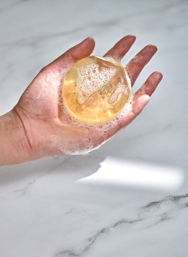 A vertical closeup shot of round glycerine soap in a hand with a foam