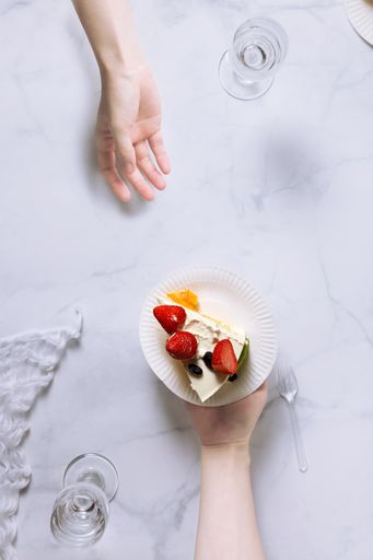 A top view shot of a person giving a plate with a piece of a strawberry cake