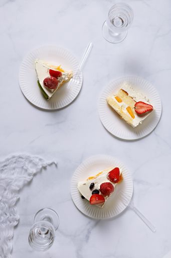 A top view shot of three plates with strawberry cake pieces on a white surface