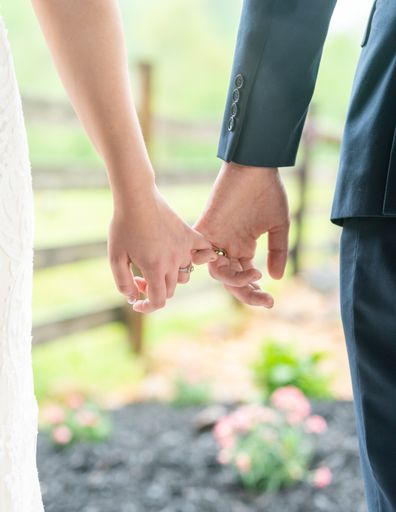 A vertical shot of a bride and a groom holding hands in a garden