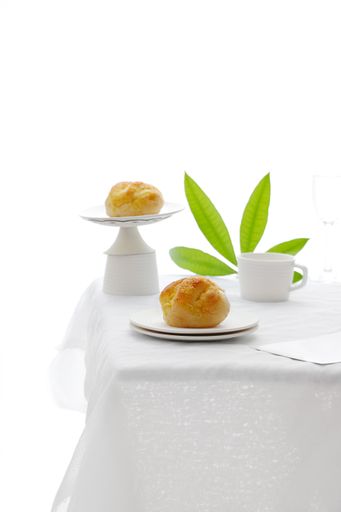 A vertical shot of a minimalistic breakfast table with teacup and two desserts on a white background