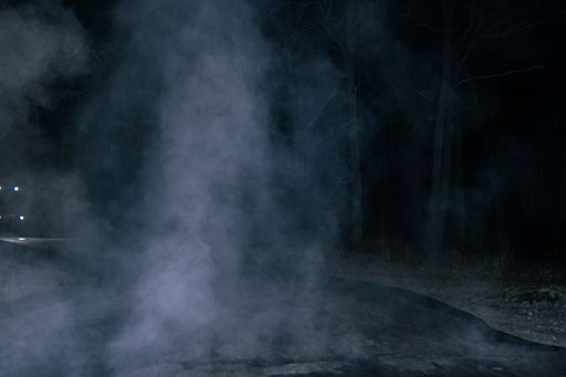 A night view of a smoke over a road in a forested area