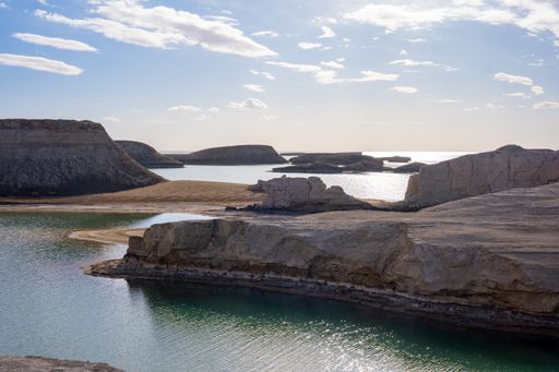 A rocky shore with a clear water under a bright cloudy sky