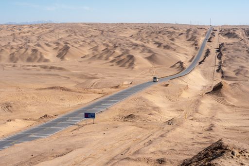 An asphalt road passing next to a deserted area under the clear sky