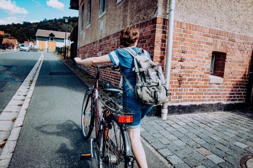 A cyclist taking his bicycle through a narrow path surrounded by old brick buildings