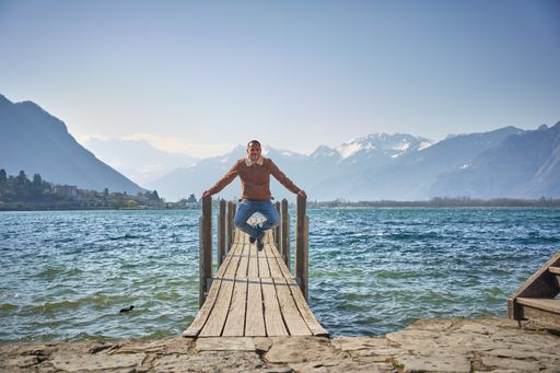 A caucasian male jumping on the jetty on the background of wavy sea and mountains in Montreux, Switzerland