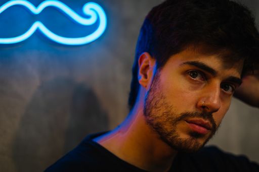 A portait of a young Caucasian male on the background of a blue mustache neon light