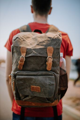 A vertical shot of a male wearing a grey leather backpack with brown details