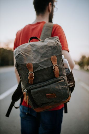 A vertical shot of a male wearing a grey leather backpack with brown details