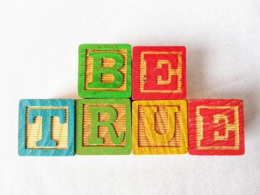 A closeup of colorful cubes spelling the word "be true" with a white background