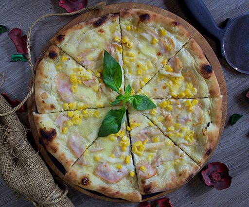 A high angle shot of a pizza with ham and corn on a wooden tray