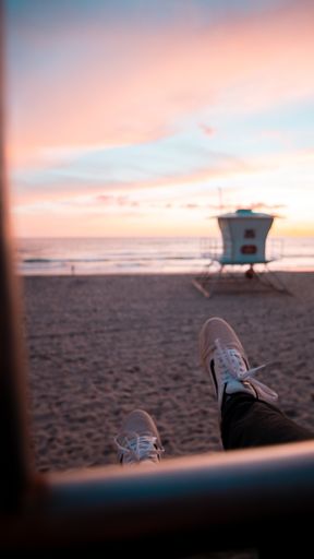 A shallow focus shot of a person wearing shoes at the beach during sunset