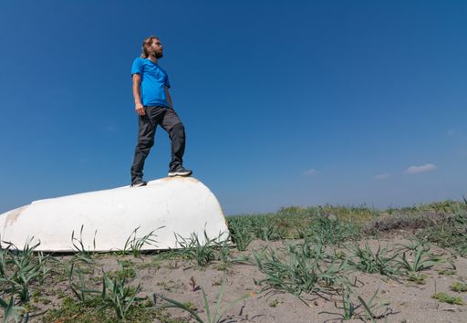 A young Caucasian male sitting on a white old bathtub in a grassy field