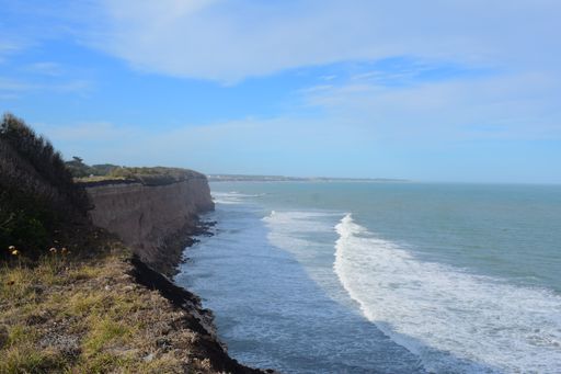 A Beautiful shot of wavy sea crashing rocky cliffs under a blue sky on a sunny day
