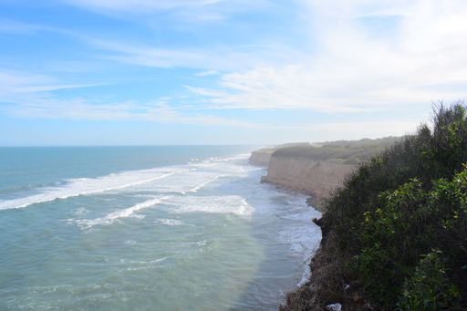 A beautiful shot of wavy sea crashing rocky cliffs under a blue sky on a sunny day