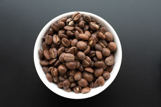 A closeup shot of coffee beans in a white bowl on a black background