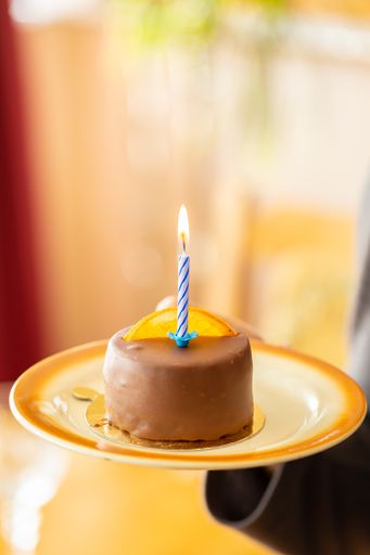 A vertical shot of a small chocolate cake with a candle in a plate in a blurred background