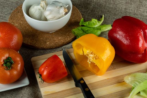 A closeup shot of colorful peppers on a wooden cutting board tomatoes and garlic in the bowl