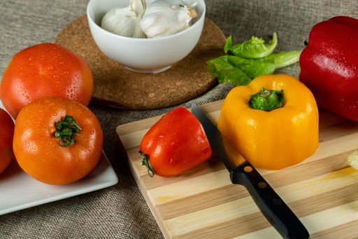 A closeup shot of colorful peppers on a wooden cutting board tomatoes and garlic in the bowl