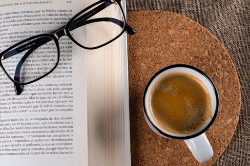 A closeup shot of a cup of coffee optical glasses and an open book