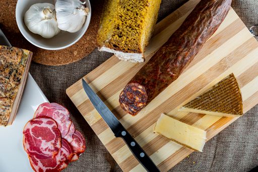 A closeup shot of a piece of parmesan cheese Ventricina sausage and bread on a cutting board