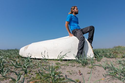 A young Caucasian male sitting on a white old bathtub in a grassy field