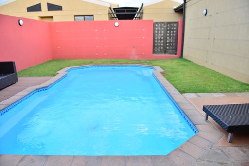 A beautiful view of a pink house with an outdoor small swimming pool and lounge chair