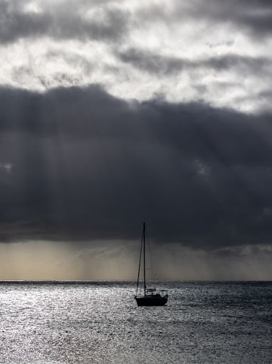 A beautiful scene of a silhouetted boat on the shiny gray water against a dramatic cloudy sky