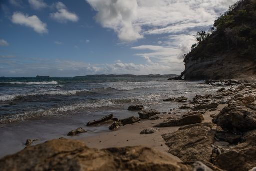 A beautiful shot of rocks on a beach and a mountain covered with green grass under the cloudy sky