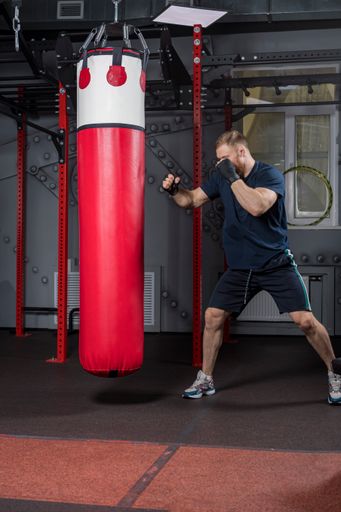 Young strong bearded man, mixed martial arts fighter and trainer, trains in gym. Stands in defensive stance in front of red punching bag.