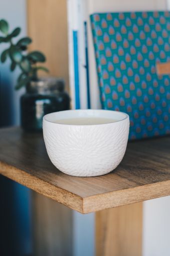 An aromatic candle on the shelf with notebooks and plant