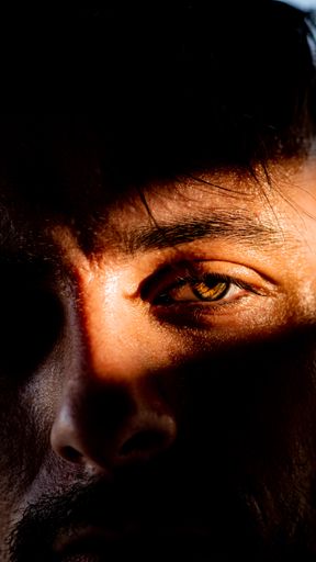 A vertical close-up shot of sunlight dripping on a human's eye.