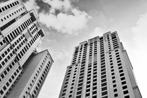 A low angle grayscale shot of tall buildings under a cloudy sky
