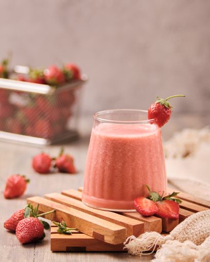 A closeup shot of a glass of fresh strawberry milkshake with strawberries on the table