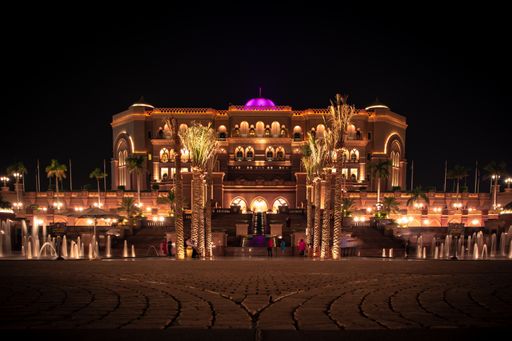 A wide shot of tropical trees and ground water fountains near Emirates Palace at night in Abu Dhabi
