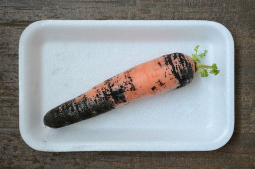 A top view of a carrot with black root rot on a single-use plate on a rough surface