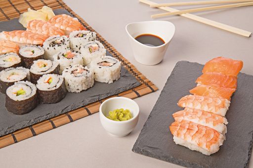 A closeup shot of a Salmon sushi set and Makizushi with a white bowl of soy sauce on the table