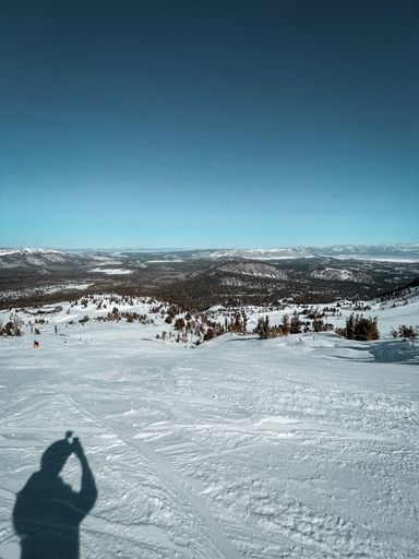 A vertical shot of a person's silhouette taking a photo of a landscape covered in snow in winter