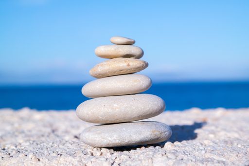 A closeup shot of pebbles stacked on each other in a balance with the blue sea in the background
