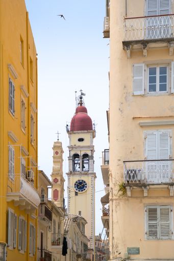 A vertical shot of a clocktower behind the buildings in Corfu, Greece