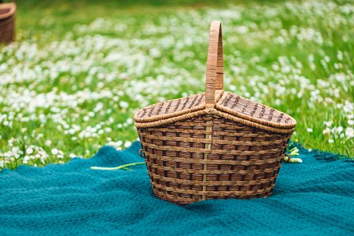 A closeup of a picnic basket on a blue cloth surrounded by white flowers