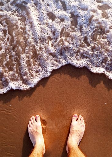 A vertical high angle shot of bare feet on the sand beach