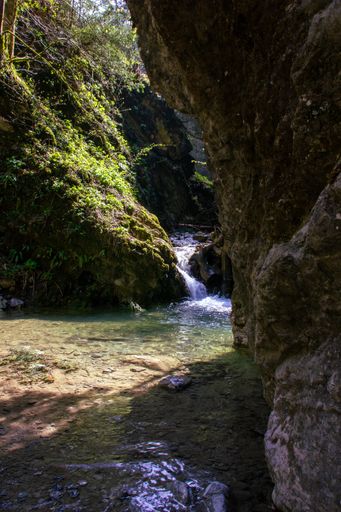 A vertical shot of a waterfall between the mossy rocks on a sunny day in spring