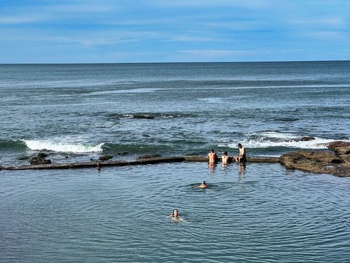 A people swim in a natural pool near the rocky coast of the sea in Australia